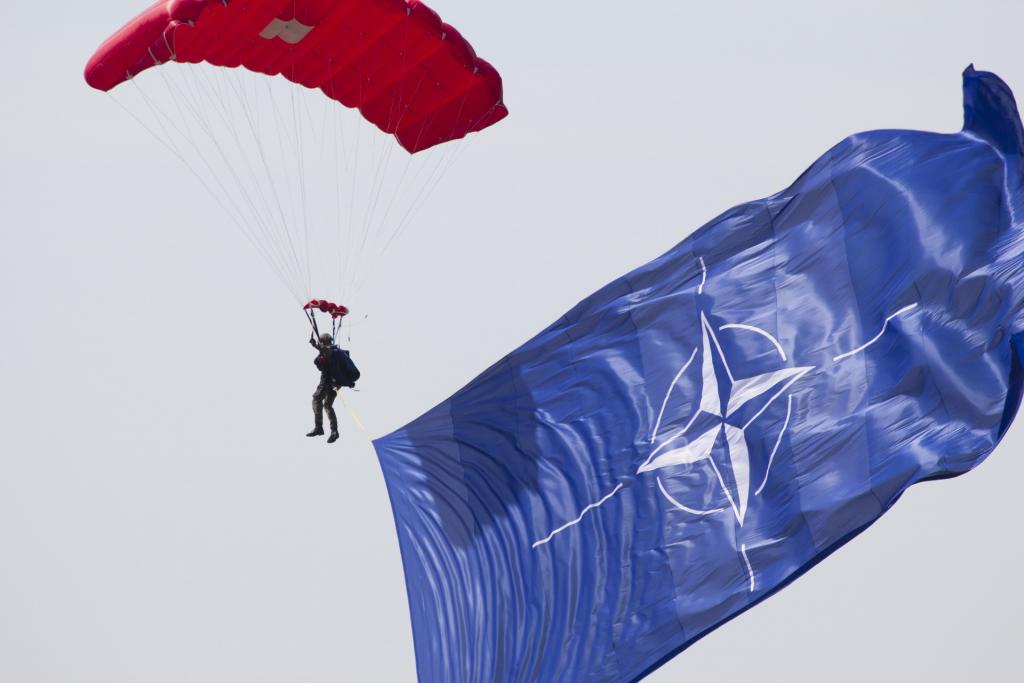 A parachuter in the sky next to NATO's flag 