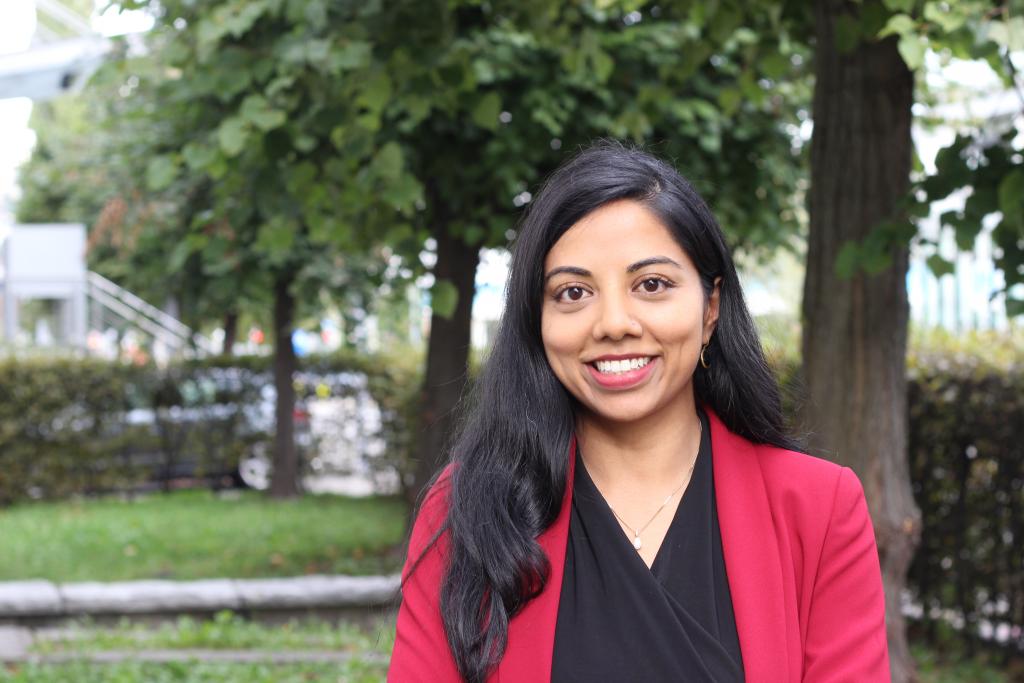 Suba smiles, standing in front of a tree-lined boulevard