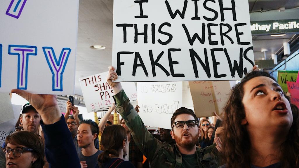 People holding a sign that reads "I wish this were fake news"