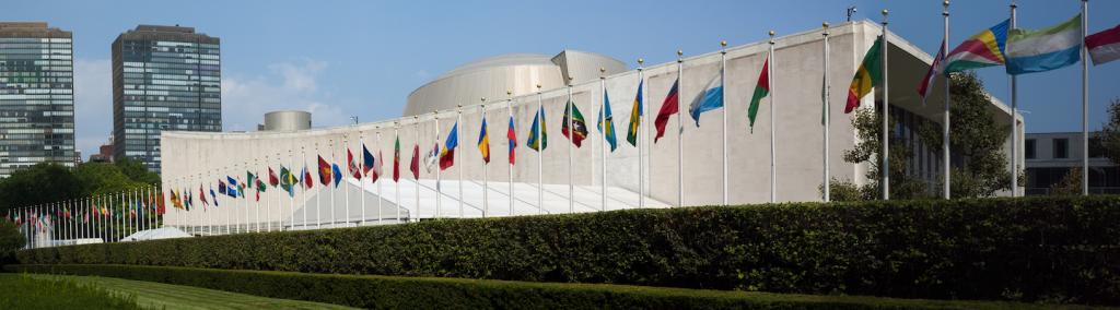 UN General Assembly, world flags flying in front, New York City.