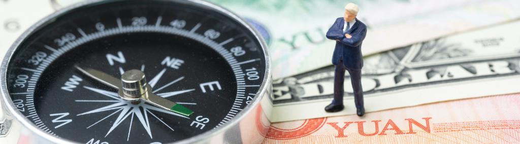 Compass with miniature leader standing on US dollar and China yuan banknotes.