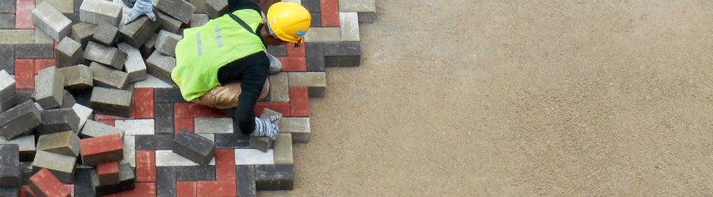 A construction worker installing precast concrete pavers stone for a road.