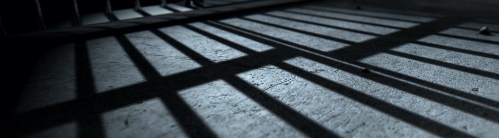 Close-up of a jail cell’s iron bars casting shadows on the prison floor.