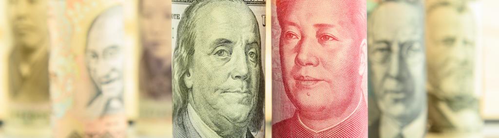 Rolled-up scrolls of USD and CNY banknotes with portraits of Benjamin Franklin and Mao Zedong on a square chessboard.