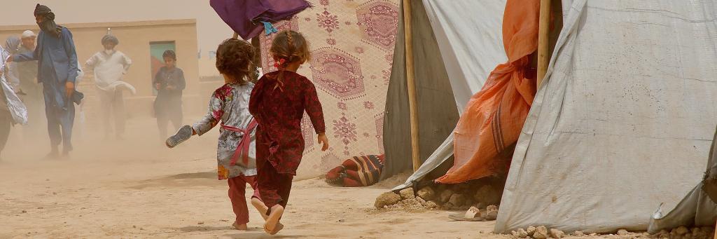 Des enfants courent pour se mettre à l’abri des tourbillons de poussière soulevés par les rafales de vent au camp de déplacés internes de Nawabad Farabi-ha.