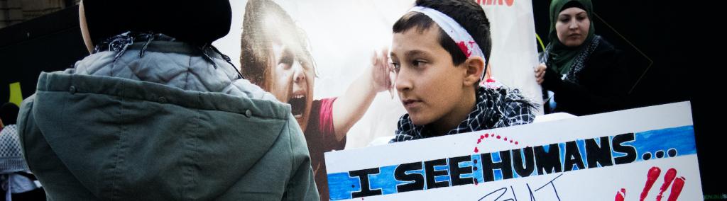 A Palestinian boy shows poster saying “I see humans but no humanity”.