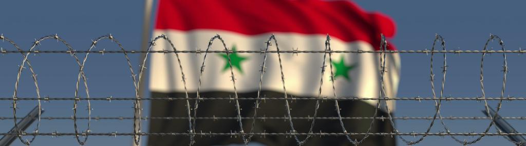 Blurred waving flag of Syria behind barbed wire fence.