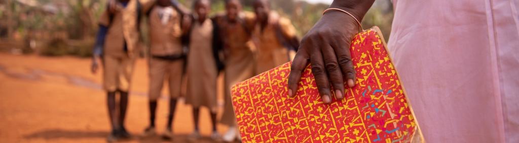 African teacher holding a book with her students out of focus in the background