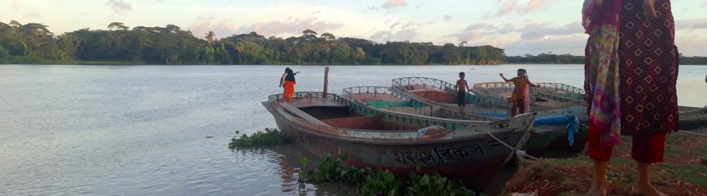 Women, children and boats on the banks of a river in Bangladesh.