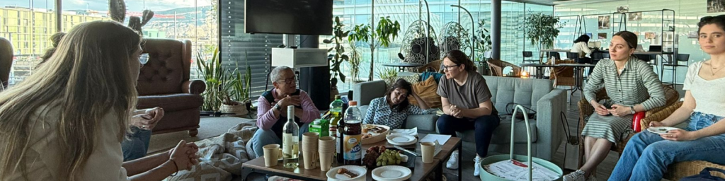 A group of people gathered in the fab. They're seated around a coffee table with drinks and snacks, engaged in conversation. The atmosphere is relaxed and friendly.