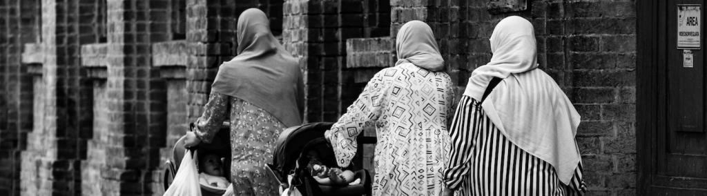 Three Muslim women walking in the street pushing baby strollers in Parma, Italy.