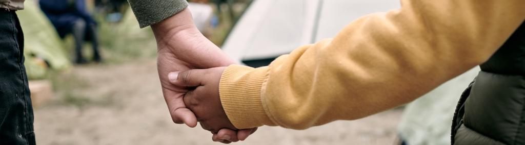 Rear view of unrecognisable children of different ages holding hands while coming into a migrant camp.