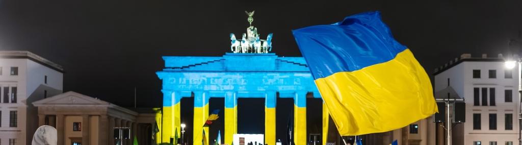 People gather near the Brandenburg Gate in Berlin, Germany, on 24 February 2026 during a pro-Ukraine demonstration marking the anniversary of Russia’s invasion of Ukraine. The landmark is illuminated in blue and yellow.