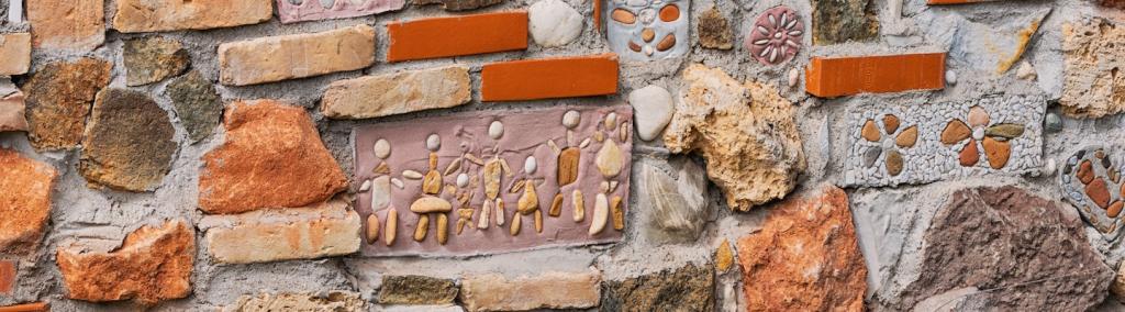Close-up view of a textured stone wall incorporating bricks, pebbles, mosaics, and decorative elements, creating a vibrant and artistic surface.