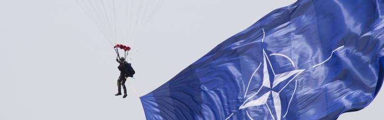 A parachuter in the sky next to NATO's flag 