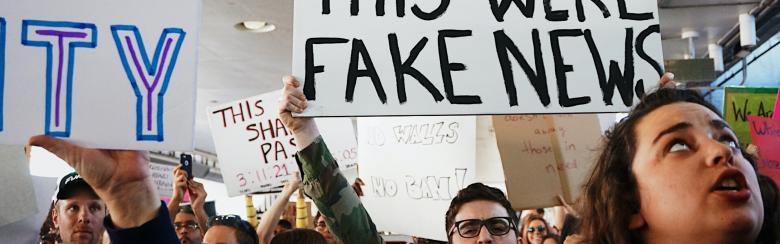 People holding a sign that reads "I wish this were fake news"