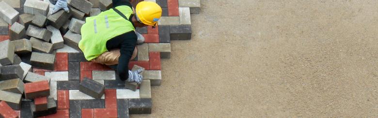 A construction worker installing precast concrete pavers stone for a road.