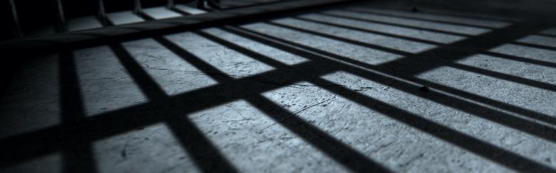 Close-up of a jail cell’s iron bars casting shadows on the prison floor.