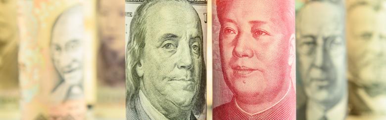 Rolled-up scrolls of USD and CNY banknotes with portraits of Benjamin Franklin and Mao Zedong on a square chessboard.