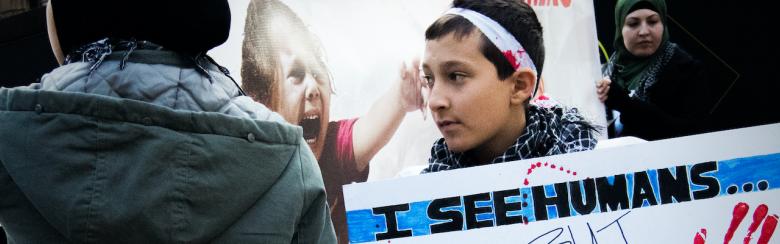 A Palestinian boy shows poster saying “I see humans but no humanity”.