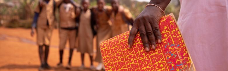 African teacher holding a book with her students out of focus in the background