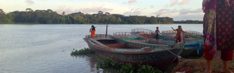 Women, children and boats on the banks of a river in Bangladesh.