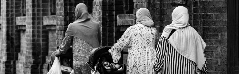 Three Muslim women walking in the street pushing baby strollers in Parma, Italy.