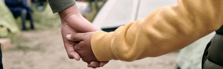 Rear view of unrecognisable children of different ages holding hands while coming into a migrant camp.