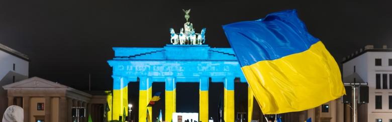 People gather near the Brandenburg Gate in Berlin, Germany, on 24 February 2026 during a pro-Ukraine demonstration marking the anniversary of Russia’s invasion of Ukraine. The landmark is illuminated in blue and yellow.