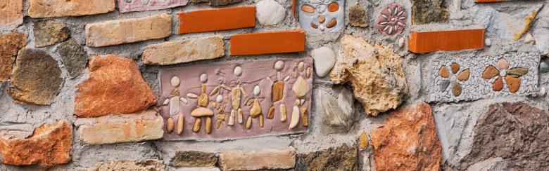 Close-up view of a textured stone wall incorporating bricks, pebbles, mosaics, and decorative elements, creating a vibrant and artistic surface.